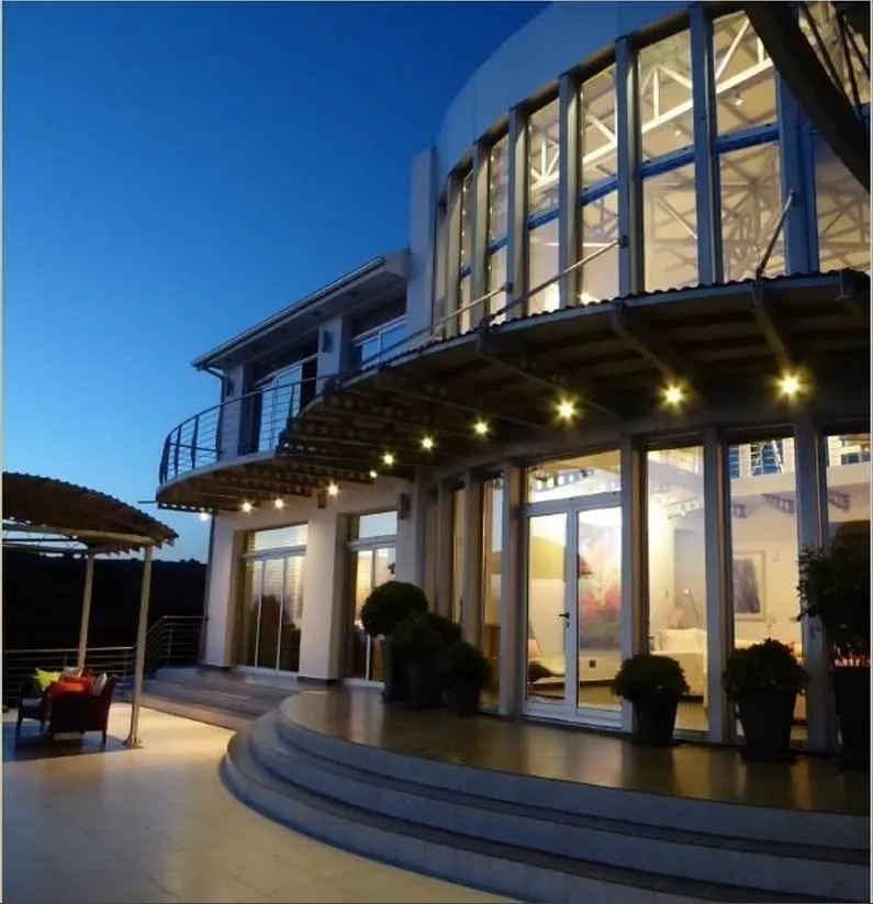 Armou residence at dusk with a curved double-height glazed façade and warmly lit terrace